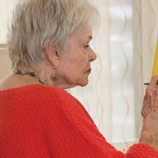 An elderly woman engaged in painting indoors.