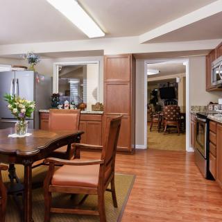 A modern kitchen with wood flooring, featuring a dining table with chairs and stainless steel appliances.