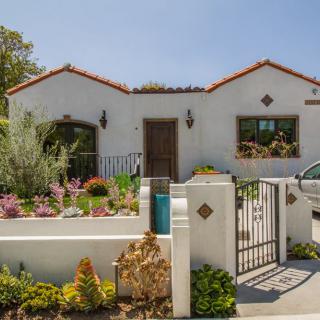 A charming house with a well-maintained garden and gated entrance on a sunny day.