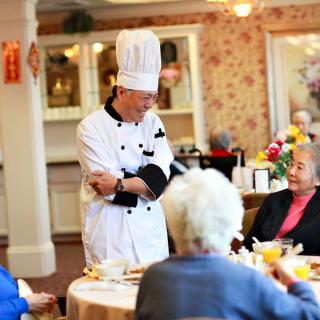 A chef interacting with senior patrons in a cozy restaurant setting.