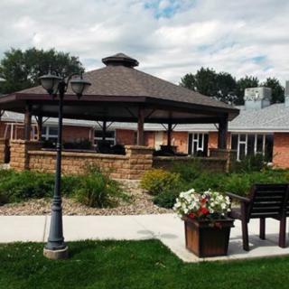 A serene garden area featuring a gazebo, surrounded by a well-maintained landscape with flowers and a bench.
