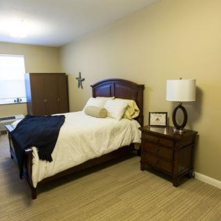 A neatly arranged bedroom with a bed, nightstand, and lamp, featuring warm tones and simple decor.