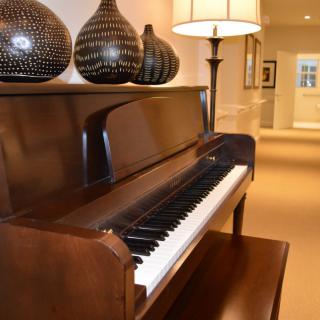 A well-decorated room featuring a polished upright piano with decorative vases and a lamp.
