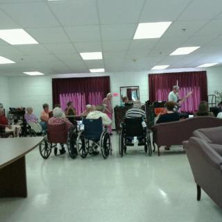 A community gathering in a nursing home with elderly residents seated in wheelchairs.