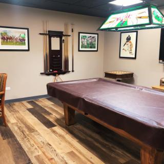 A cozy game room featuring a pool table with a cover, surrounded by framed artwork and warm wood flooring.