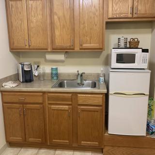 A compact kitchen area with wooden cabinets, a sink, a microwave on top of a mini fridge, and a coffee maker.