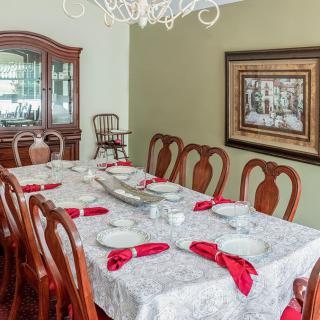 A formal dining room with an elegantly set table featuring red napkins and a chandelier overhead.