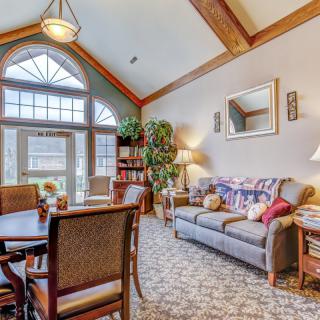 A cozy living room featuring a sofa, dining table with chairs, and decorative elements like plants and a mirror.