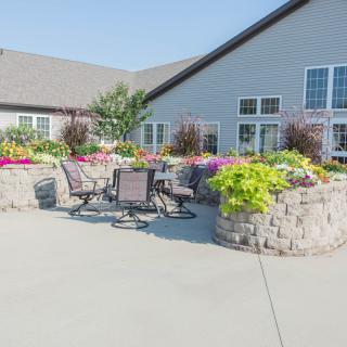 A sunny outdoor patio area with tables, chairs, and vibrant flower arrangements next to a building.
