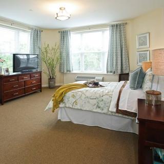 Spacious bedroom with a neatly arranged bed, television, and large windows.