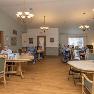 A nursing home dining area with tables, chairs, and residents seated during meal time.