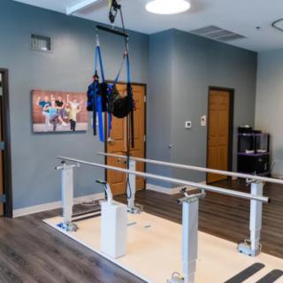 A physical therapy room equipped with parallel bars and a harness system for rehabilitation exercises.
