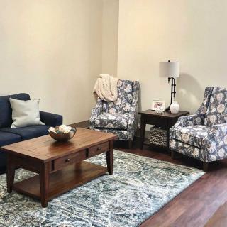 A cozy living room setup with a blue sofa, floral armchairs, a wooden coffee table, and a decorative rug.