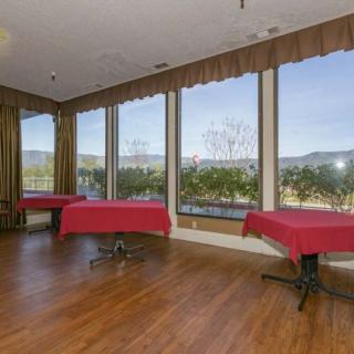 A spacious event room with large windows and red tablecloths offering views of the outdoors.