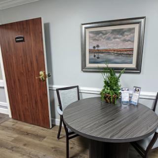 A cozy waiting area featuring a round table, chairs, and a piece of artwork on the wall.