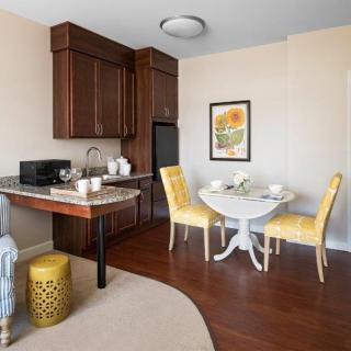 A compact kitchen and dining area featuring modern furniture, a small dining table with yellow chairs, and a hardwood floor.