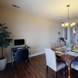 A dining room with a table set for a meal, featuring a home office corner with a computer desk.