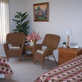 A cozy living room area with two wicker chairs, a small table, and decorative elements like a lamp, painting, and indoor plant.