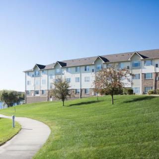A well-maintained apartment complex surrounded by green lawns and a winding pathway on a clear, sunny day.