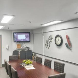 A modern conference room with a long meeting table, chairs, a wall-mounted television, and clock.