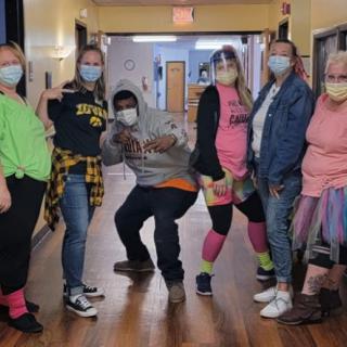 A group of people wearing masks and casual clothing pose together in a hallway.