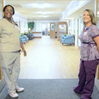 Two healthcare professionals standing in a hallway, smiling.