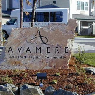 A stone sign for Avamere Assisted Living Communities in front of a building with landscaped surroundings.