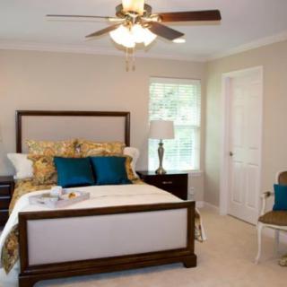 A cozy bedroom featuring a stylish bed with teal pillows, a bedside lamp, and a ceiling fan.