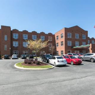 A modern brick building with a parking lot filled with various vehicles under a clear blue sky.