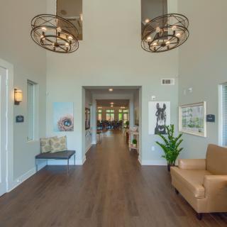 A modern lobby featuring stylish chandeliers, a seating area, and a wooden floor leading into a hallway.