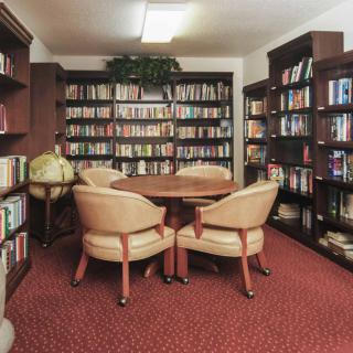 A cozy library corner with bookshelves filled with books and a reading area featuring chairs and a table.
