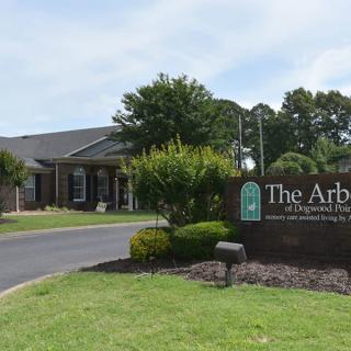 A brick building with a sign reading 'The Arbors' surrounded by well-maintained landscaping.