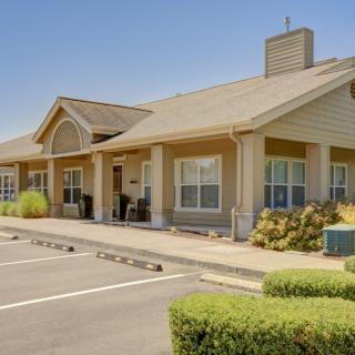 A suburban residential building with a parking lot in front, surrounded by neatly trimmed bushes under a clear sky.