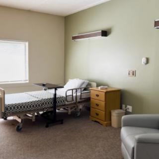 An empty hospital room with a bed and basic furniture, bathed in natural light.