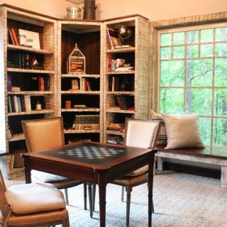 A cozy library corner with bookshelves, a chess table, and a window seat.