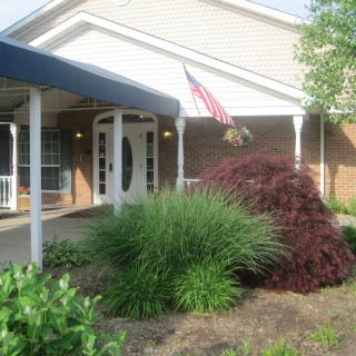 A building entrance with a porch, an American flag, and landscaped greenery.