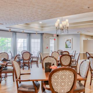 An elegant dining area with classic wooden chairs, a chandelier, and large windows letting in natural light.
