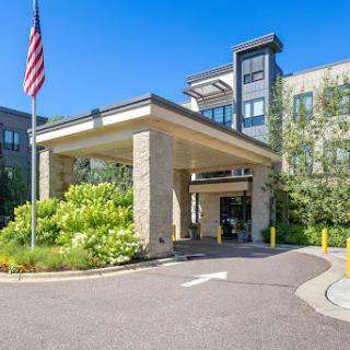 The welcoming entrance of a modern hotel with well-kept landscaping and an American flag prominently displayed.