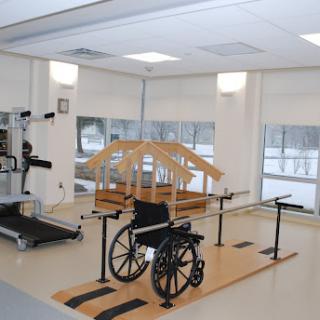 A rehabilitation therapy room featuring a wheelchair, wooden balance training structure, and physical therapy equipment.