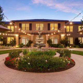 A beautifully lit courtyard features a central fountain surrounded by lush gardens at dusk.