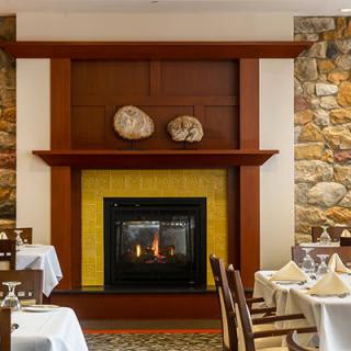 A cozy restaurant dining area featuring a central fireplace and elegantly set tables.