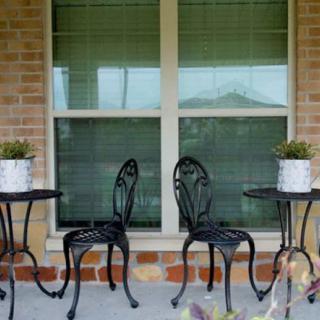 A cozy patio setup with black metal chairs and tables, decorated with potted plants against a brick wall and window backdrop.