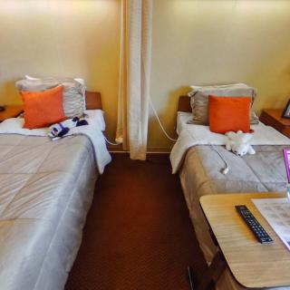 A cozy hotel room with twin beds and orange accent pillows.