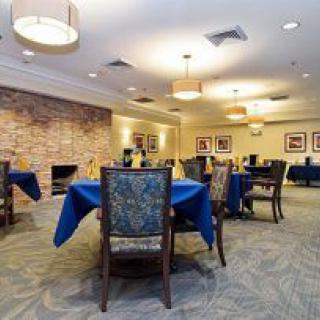 A well-lit dining room with tables covered in blue tablecloths and a brick accent wall.