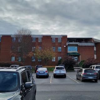 A view of an apartment complex with a parking lot full of cars under a cloudy sky.