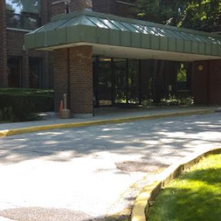The entrance of a building with a covered awning and surrounding greenery.