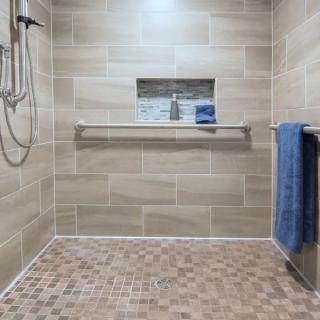 A modern walk-in shower featuring beige wall tiles, a niche shelf with toiletries, and a blue towel on a towel rack.