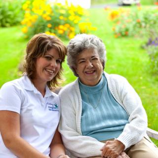 A younger woman and an elderly woman smiling together in a garden.