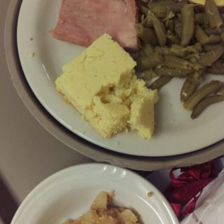 A meal consisting of ham, green beans, cornbread, and mashed potatoes on a plate.