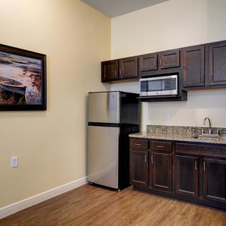 A compact kitchen area with dark wood cabinets, stainless steel refrigerator and microwave, and a small countertop and sink.